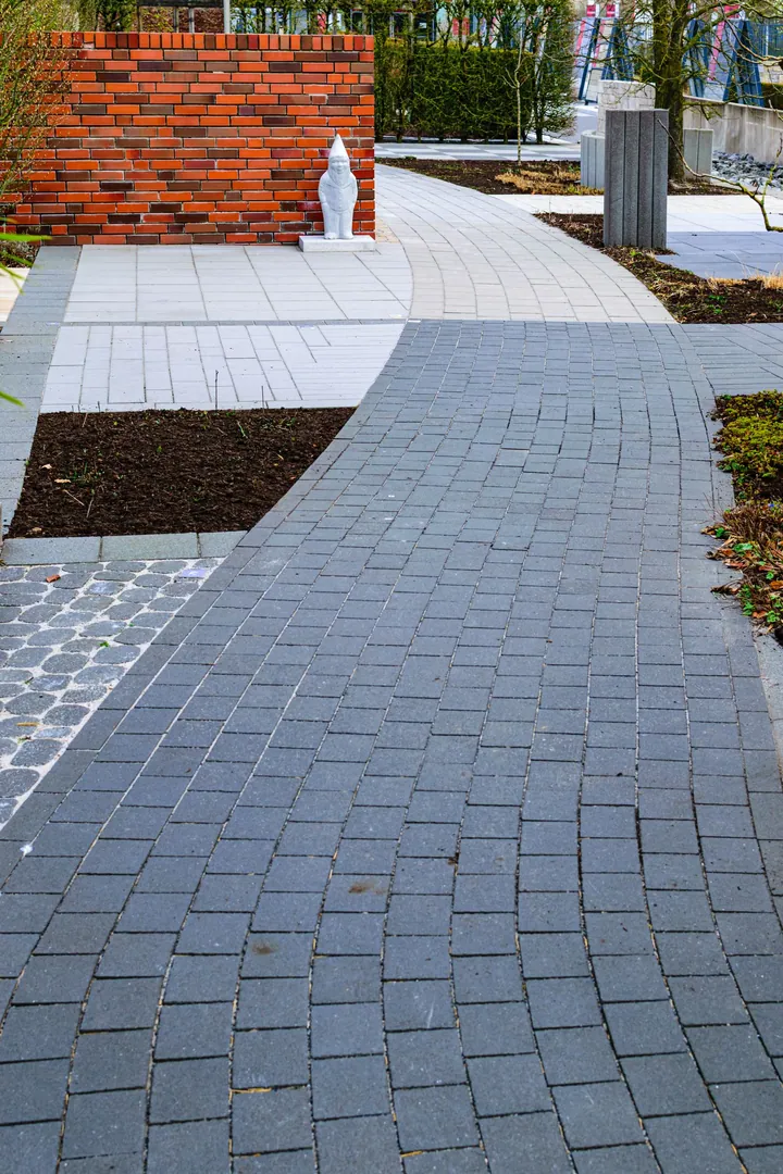 A grey paved garden walkway beside a lawn and a white fence