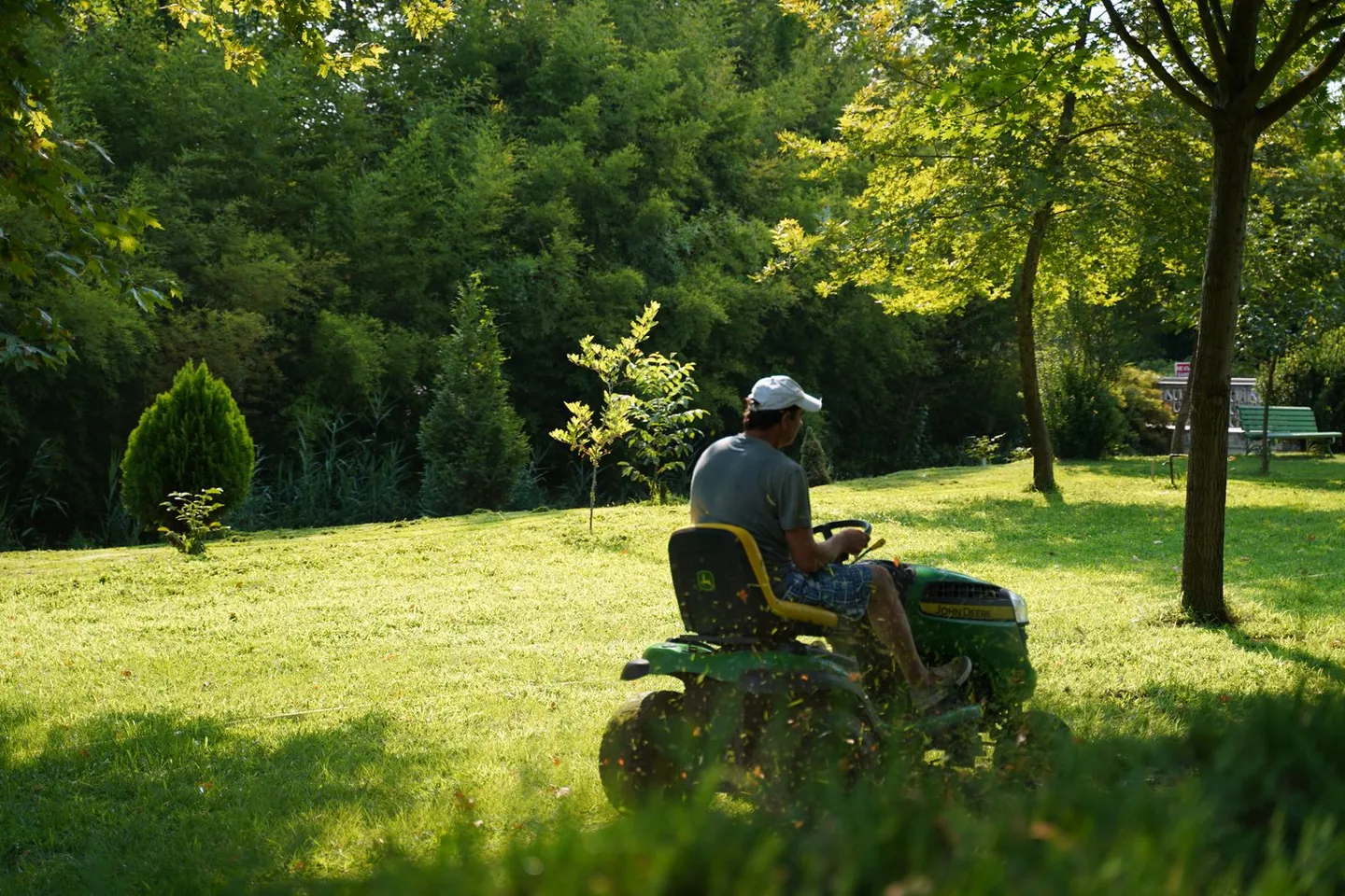 A green lawn surrounded by trees, with a mower in the distance