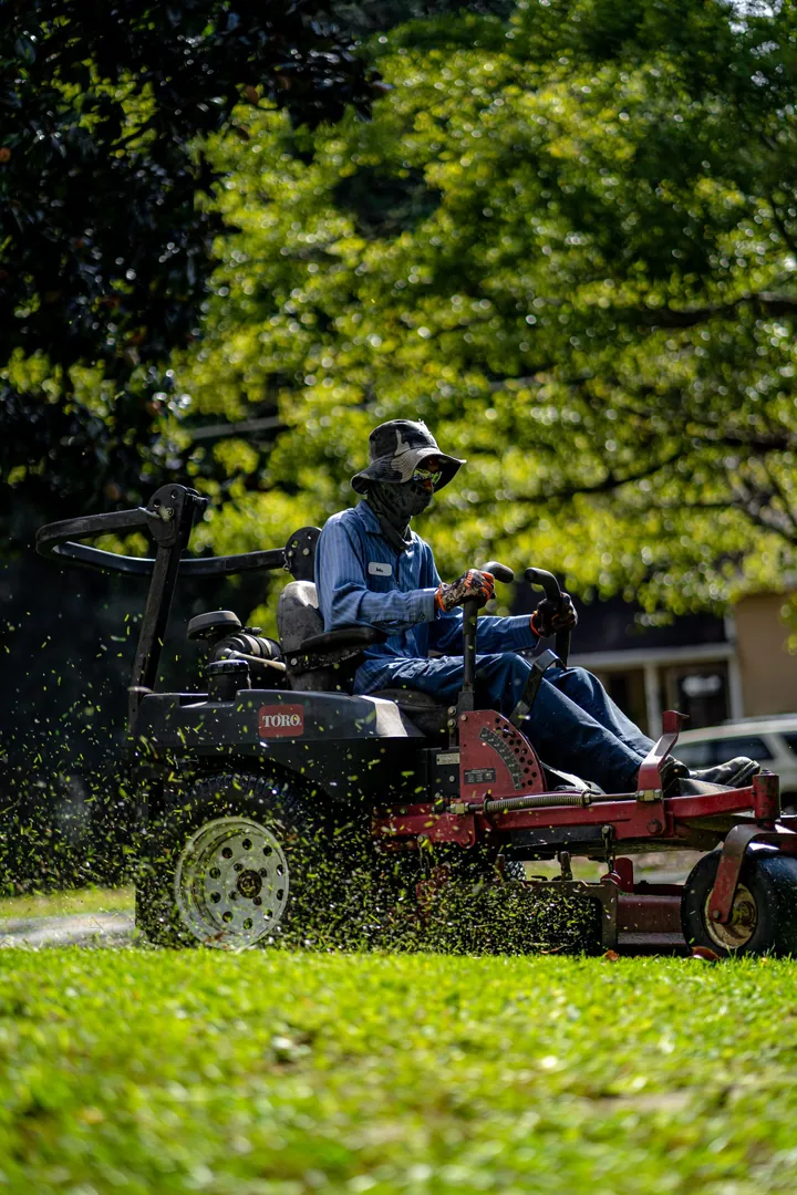 A mower working on grass beside trees